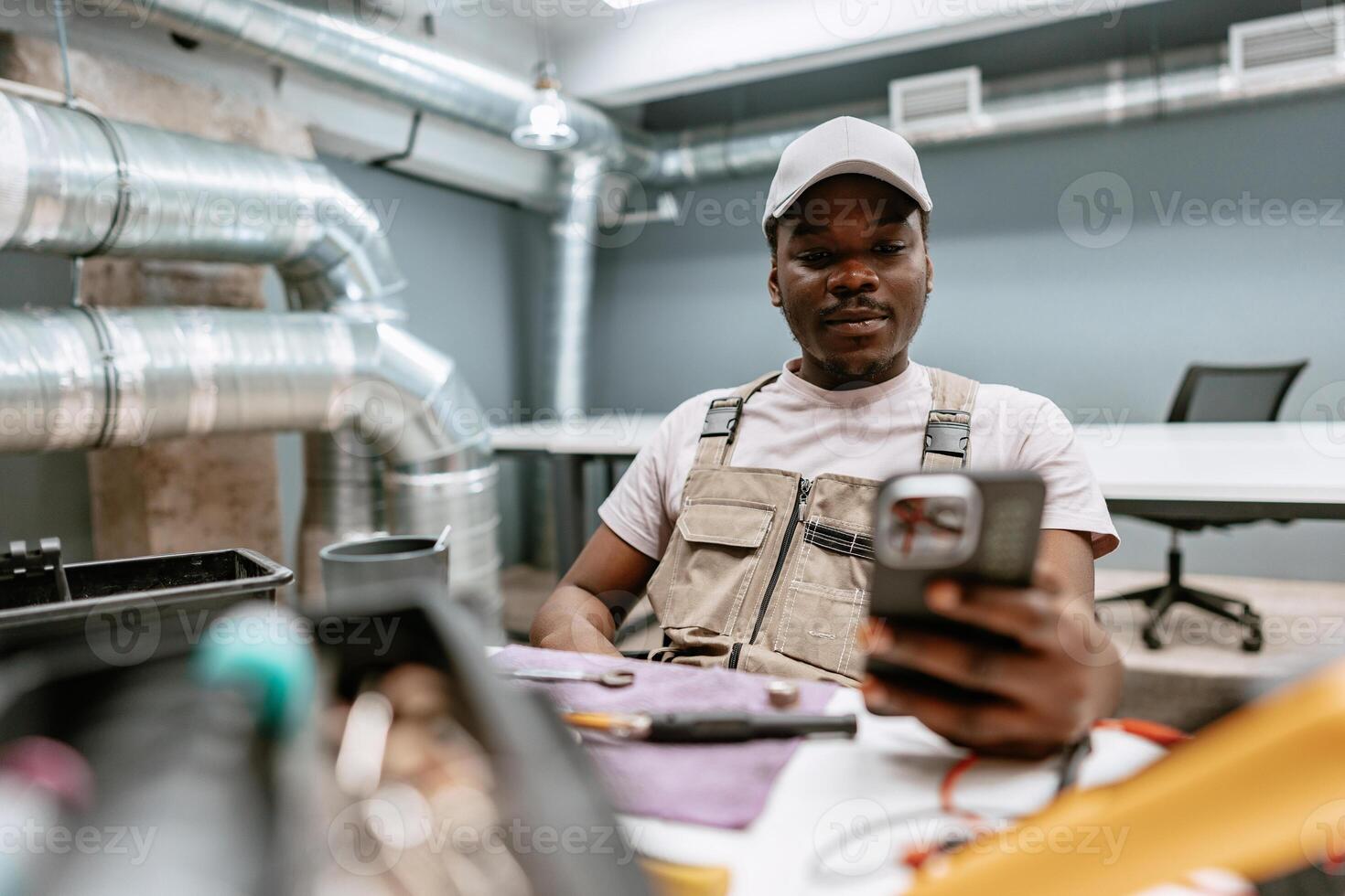 Skilled worker checking smartphone while seated in a modern workspace with exposed ductwork photo