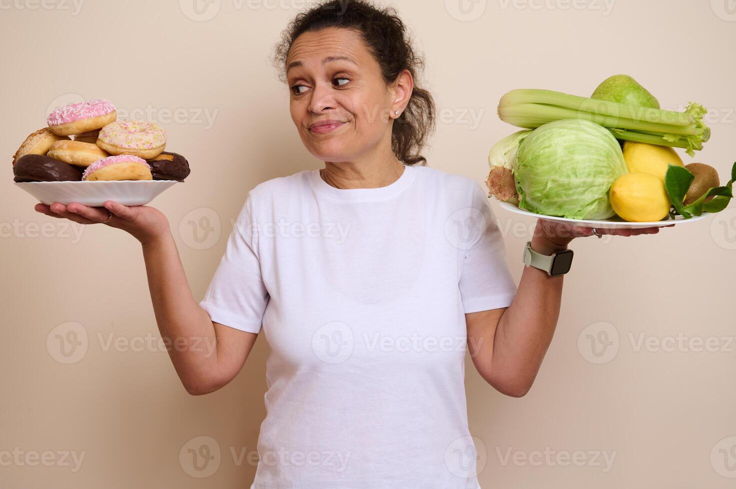 Balanced Choices. Woman Weighing Plates of Doughnuts and Fresh Vegetables photo