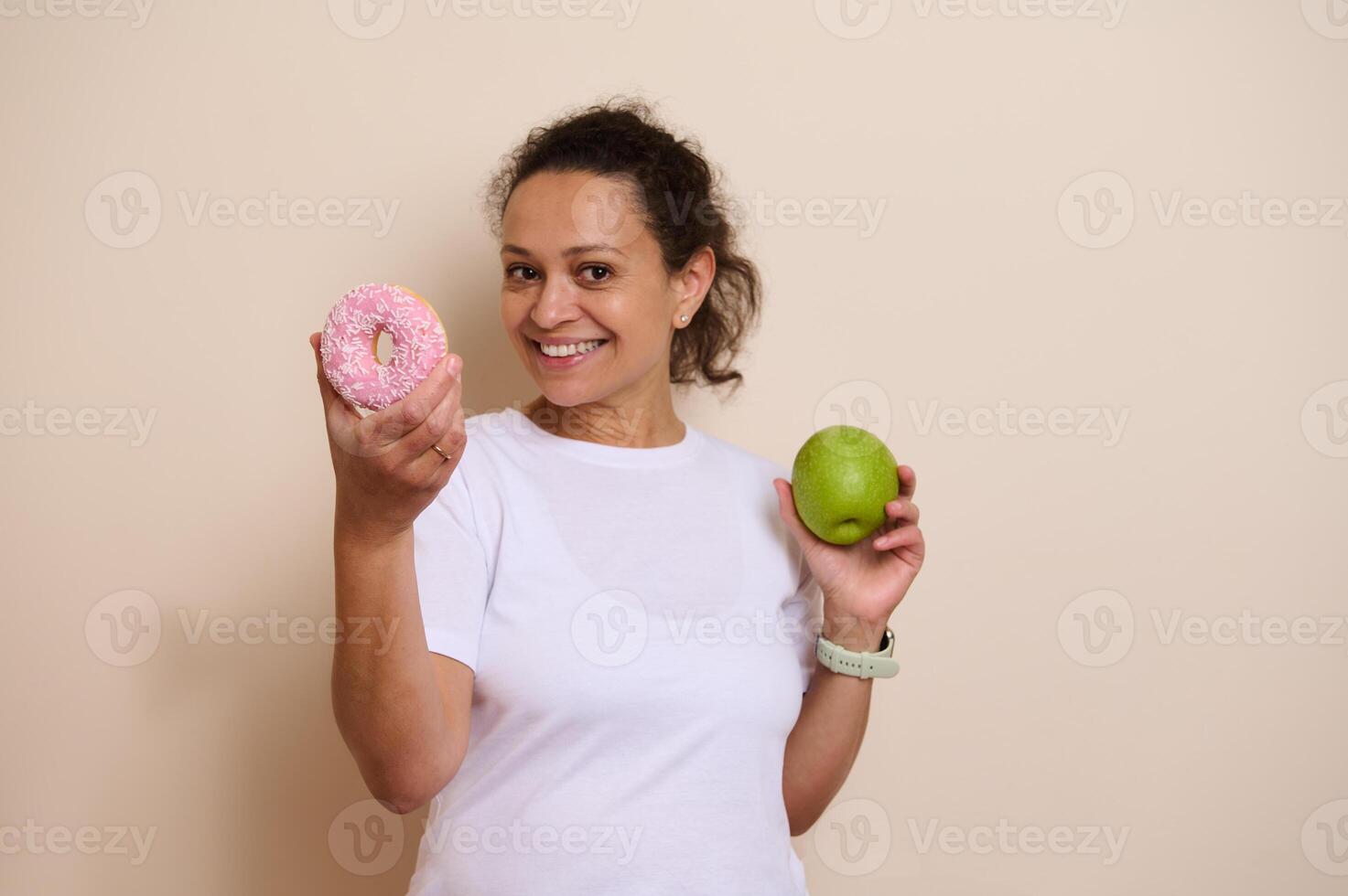 Smiling Woman Comparing a Green Apple and a Pink Frosted Doughnut photo
