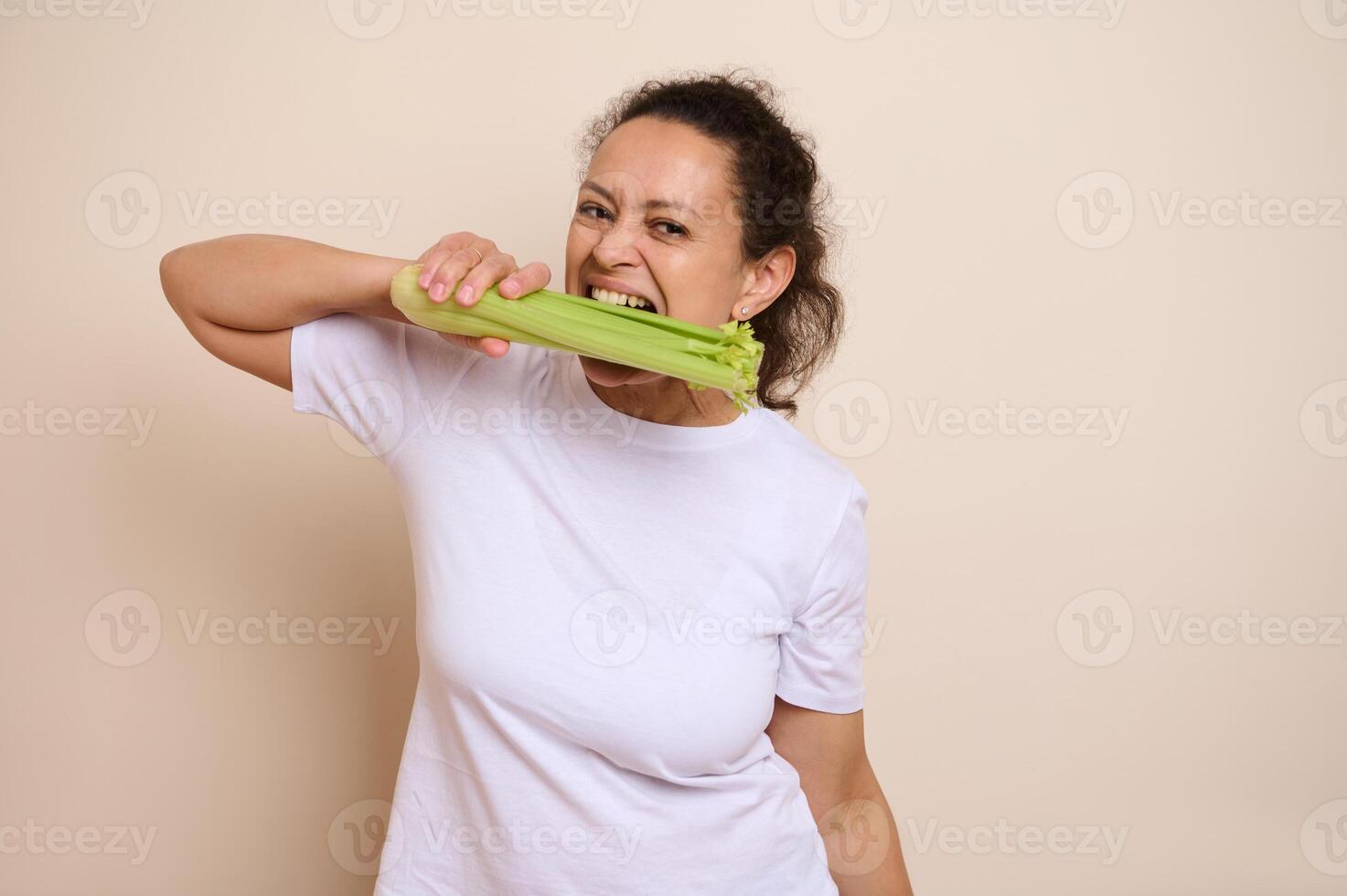 Woman Demonstrating Healthy Eating by Biting into a Fresh Celery Stalk in a Neutral Setting photo