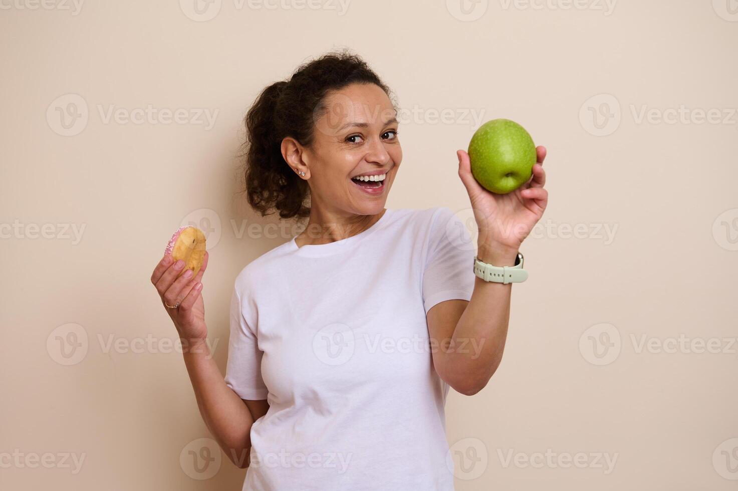 Smiling Woman Holding a Green Apple in One Hand and a Doughnut in the Other, Representing a Healthy vs. Indulgence Choice photo
