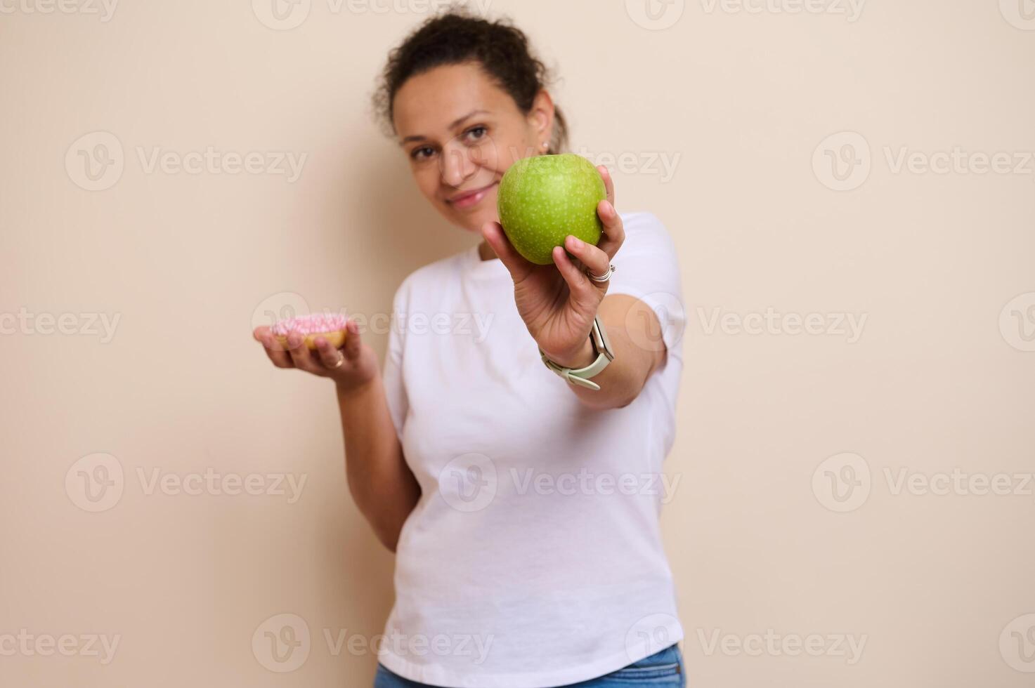 Woman Comparing a Green Apple and a Pink Frosted Donut Emphasizing Healthy Choices photo