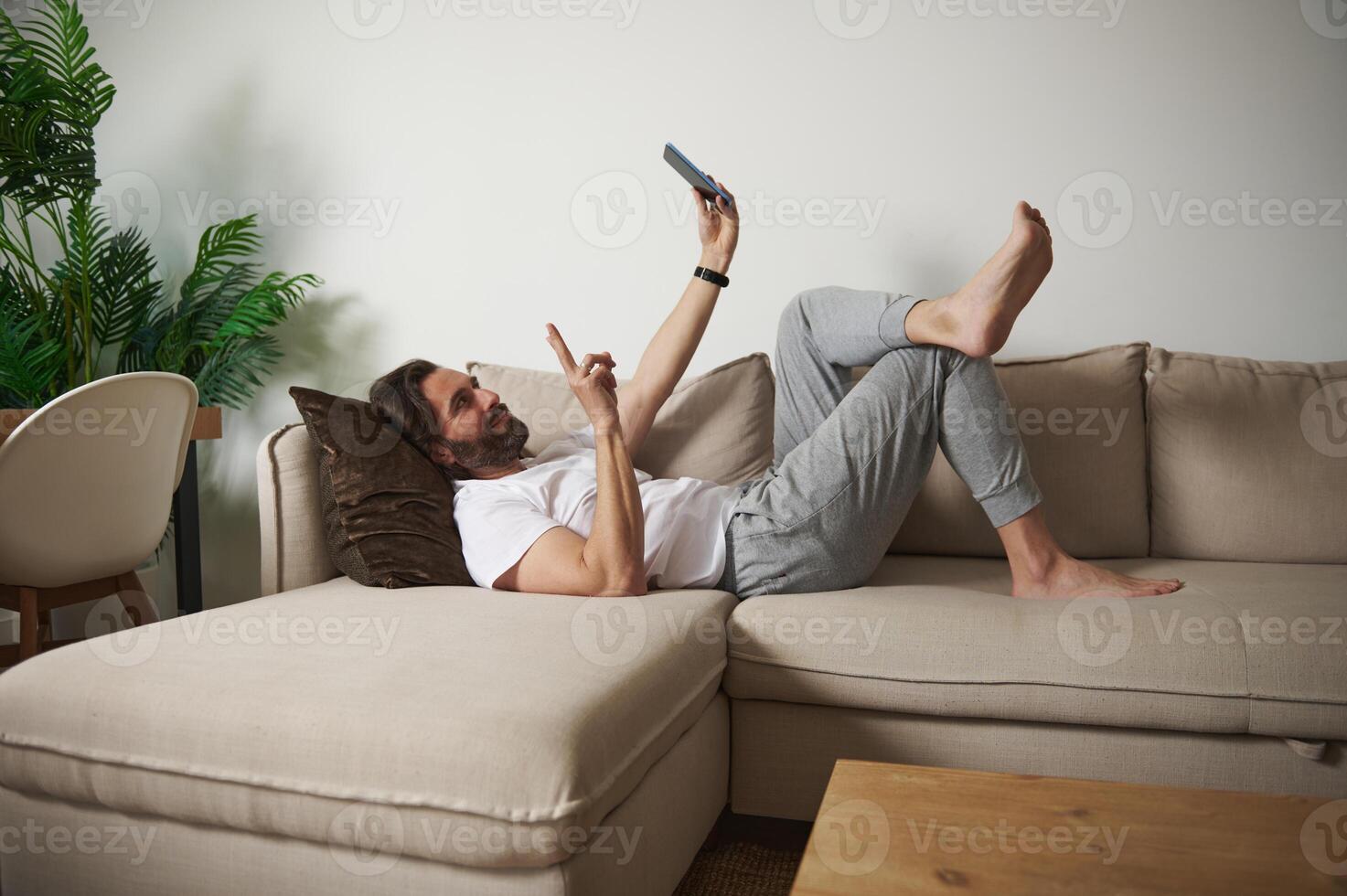 Man Relaxing on Couch Using Smartphone in Cozy Home Interior photo