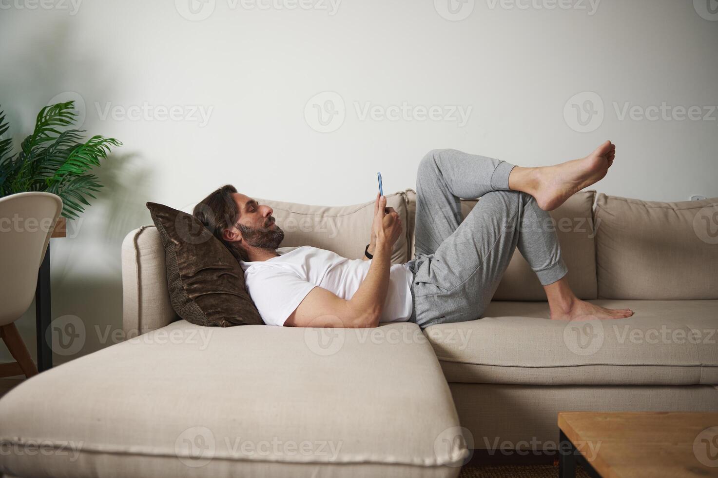 Man Relaxing on a Comfortable Sofa While Using a Smartphone in a Modern Home Setting photo