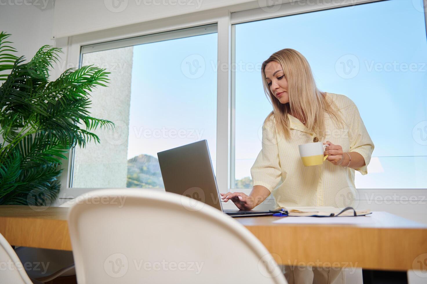 Home Office Setup Featuring Woman Working Remotely with Laptop and Coffee photo