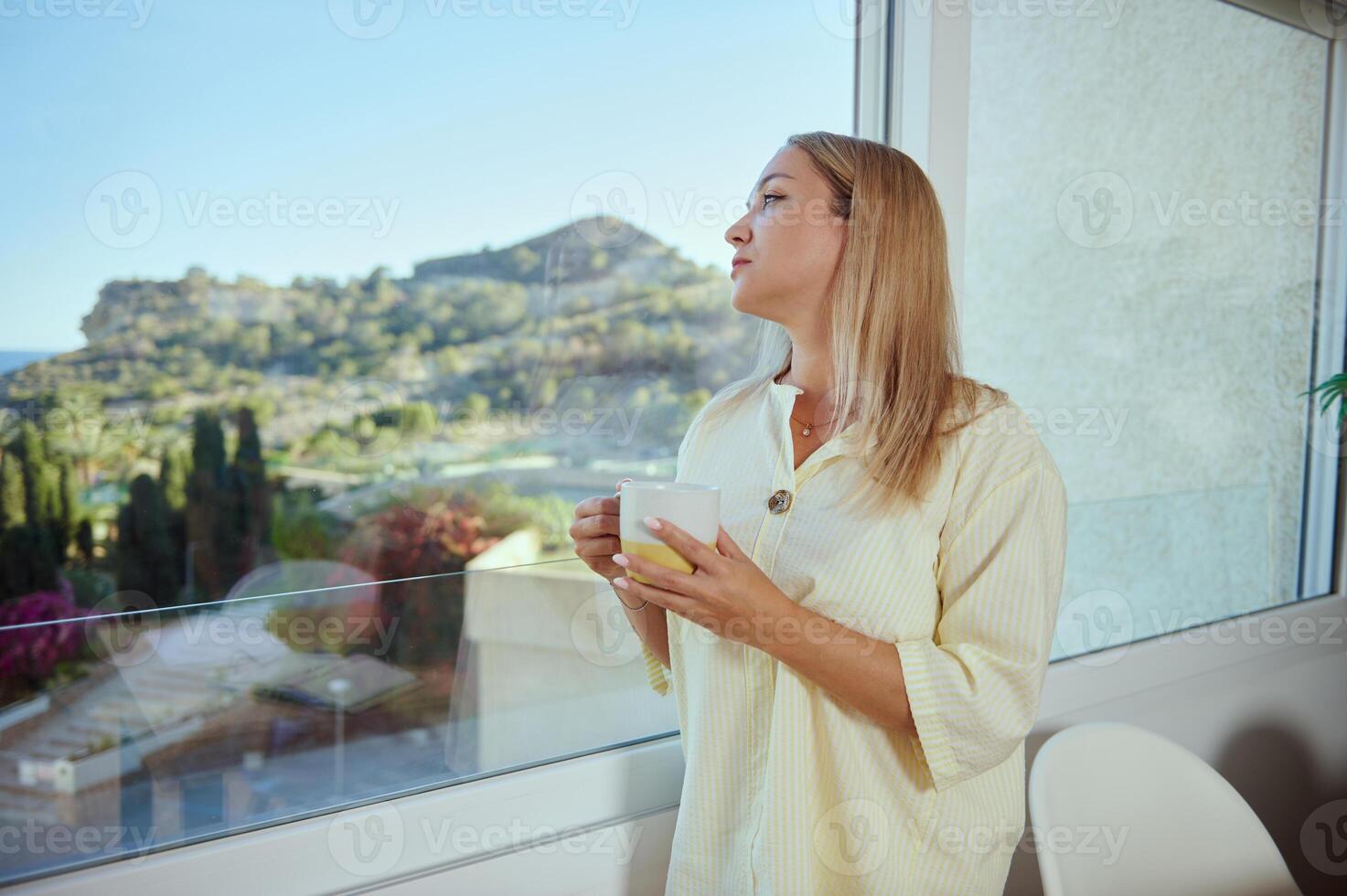 Woman Enjoying a Scenic View While Sipping Coffee at Home in Bright Natural Light photo