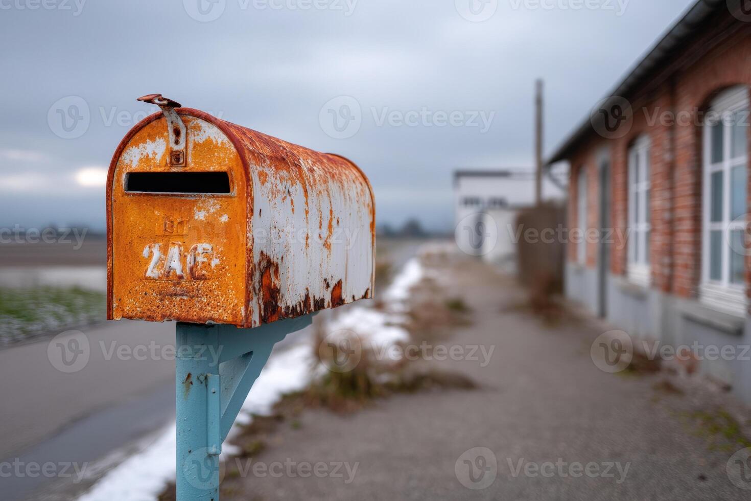 Rusty mailbox stands by an old building on a quiet path during cloudy day photo