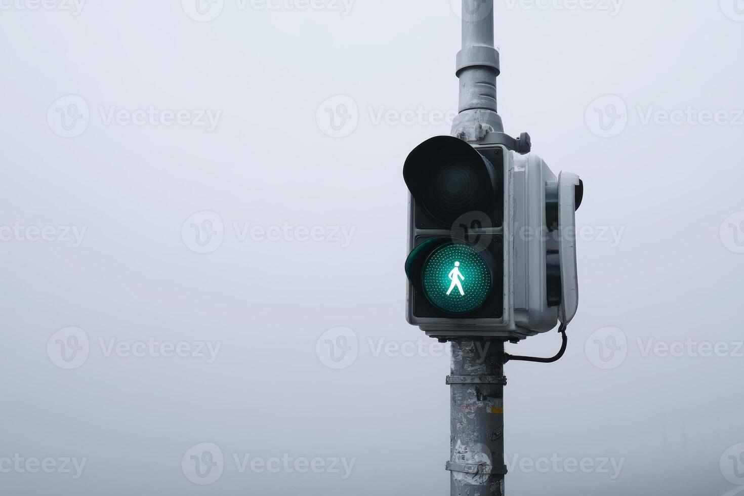Green pedestrian signal shining in a foggy urban environment during early morning hours photo
