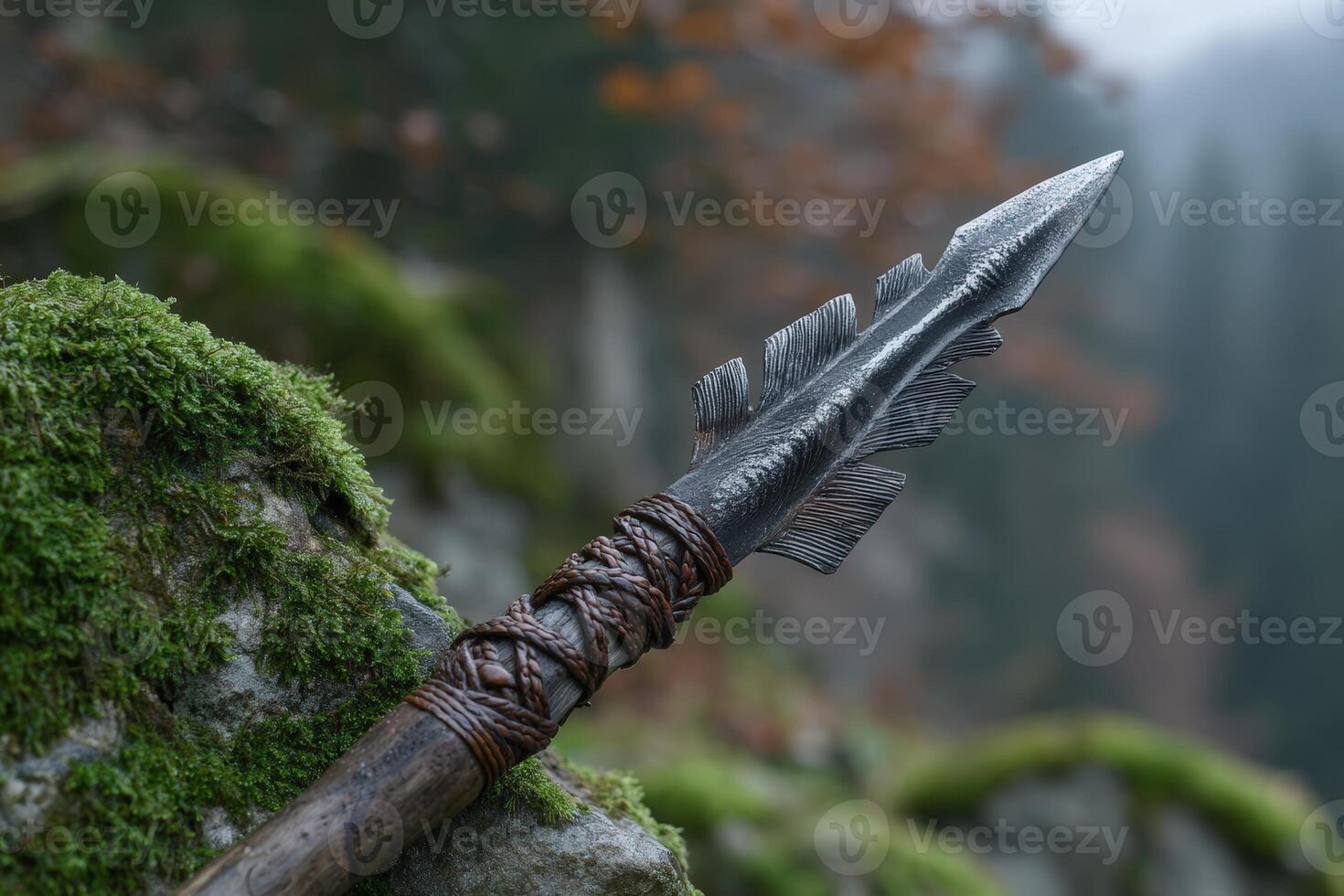 Sharpened obsidian tip spear with braided handle resting on mossy rocks in a misty forest photo