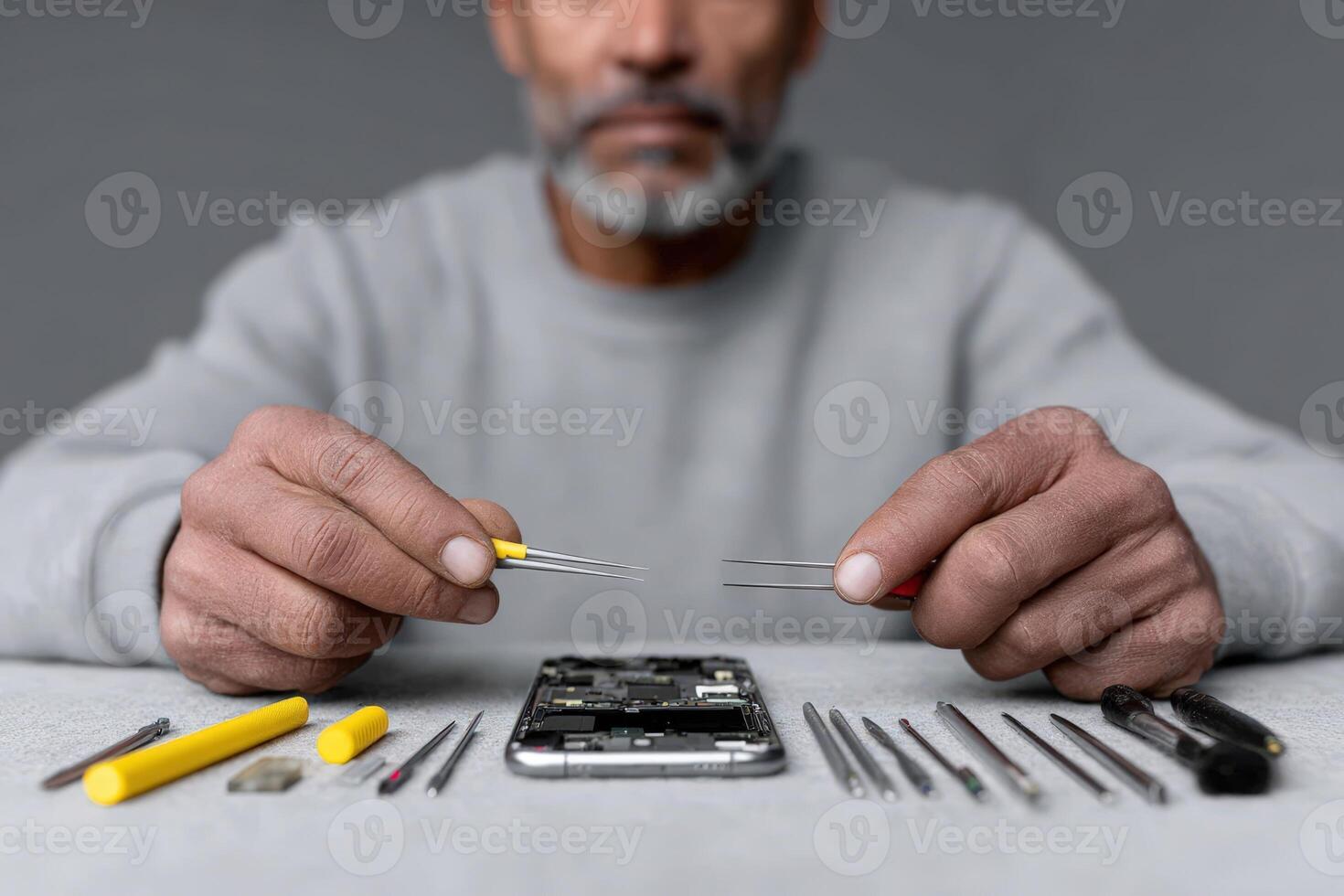 Hands hold miniature tools while repairing a smartphone on a work surface photo