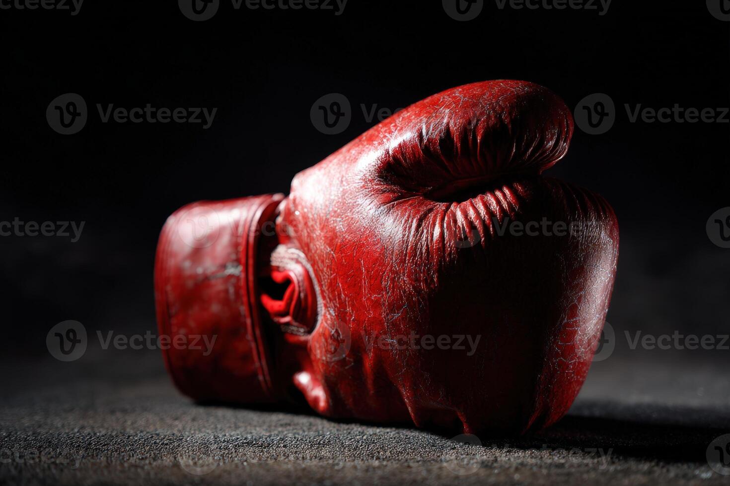 Red boxing glove resting on dark surface with shadows highlighting its worn appearance photo