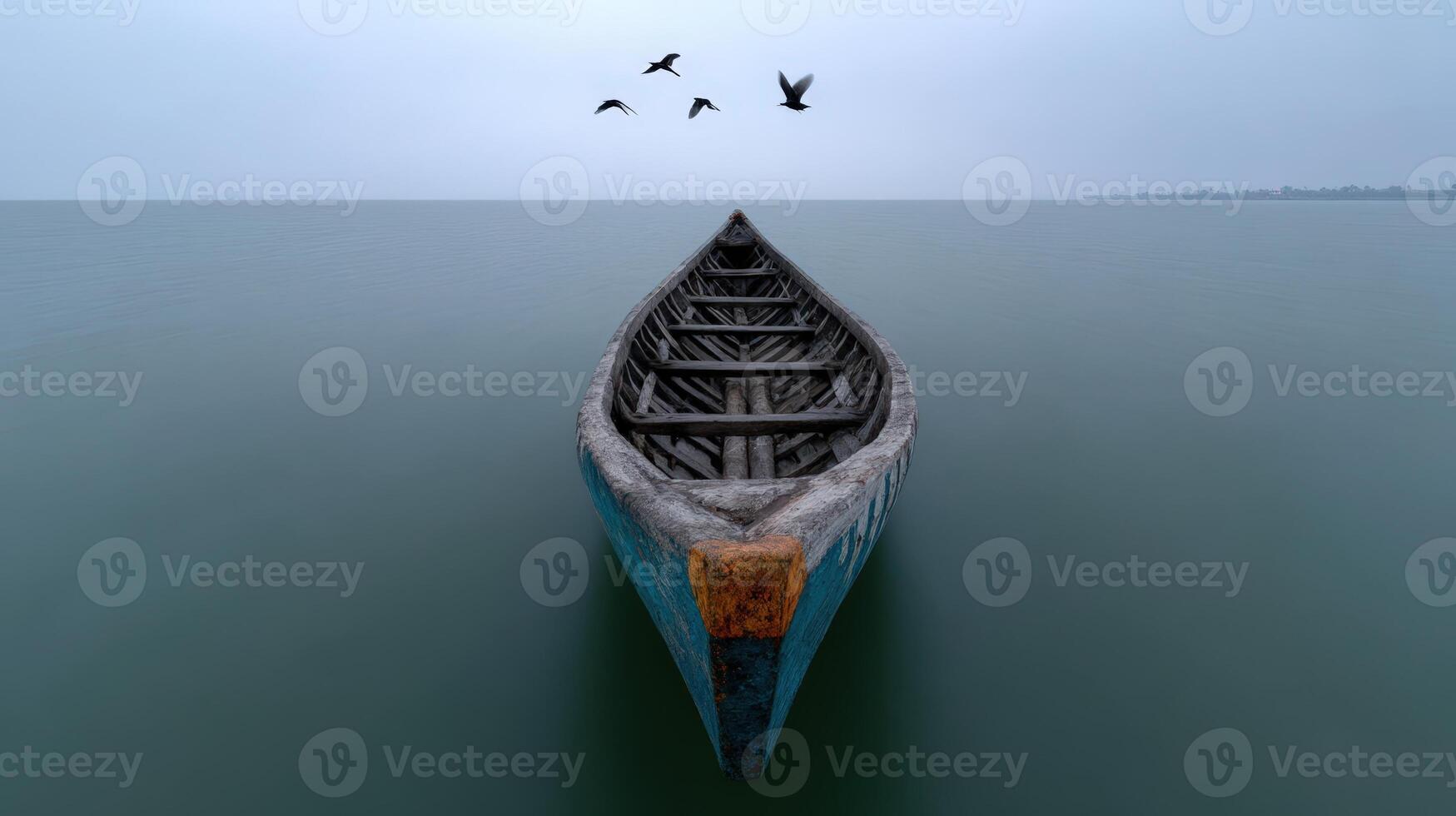 Canoe floating peacefully in calm sea under gray sky with birds flying above photo