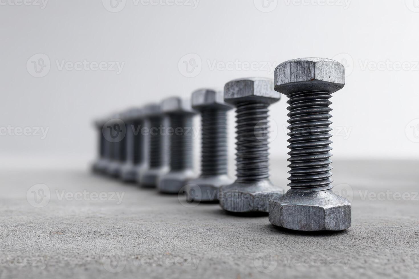 Row of steel bolts arranged with precision on a concrete surface in a workshop setting photo