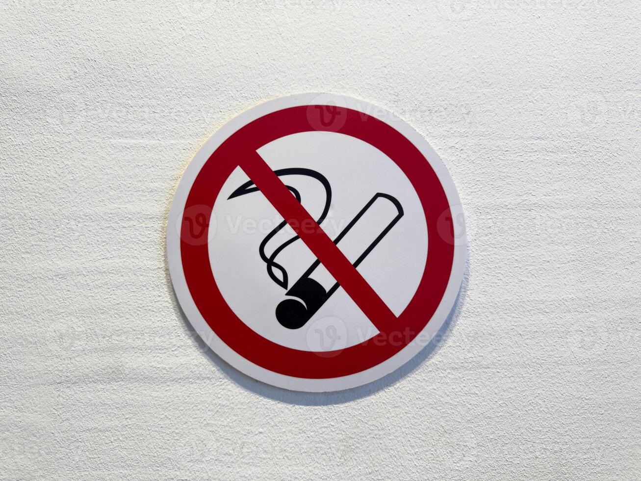 Close up of no smoking sign on white wall. Red circle with cigarette symbol and diagonal line emphasizes public health, safety and clean air in indoor environments photo