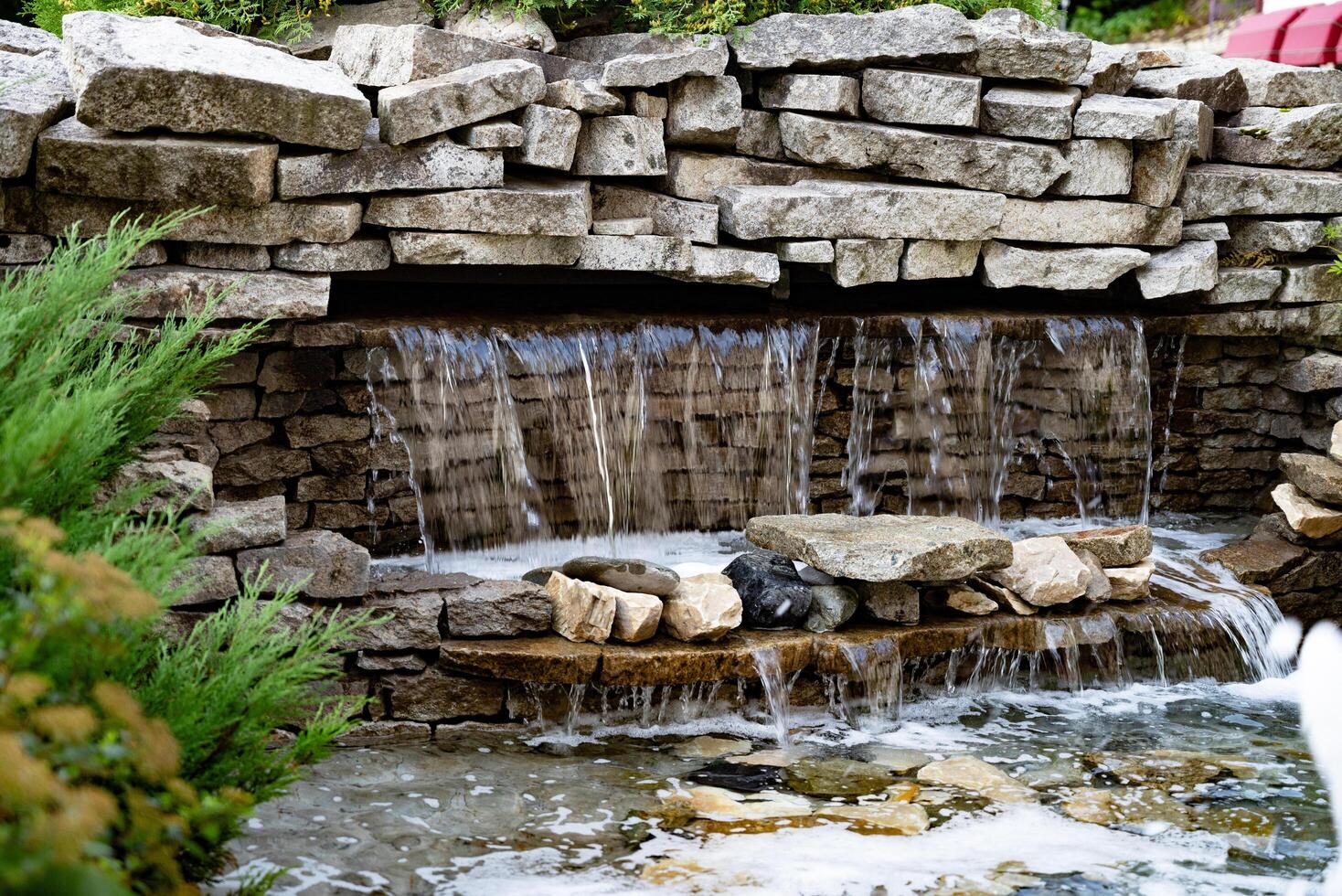 Beautiful garden with stone waterfall and fountain in front of building. photo