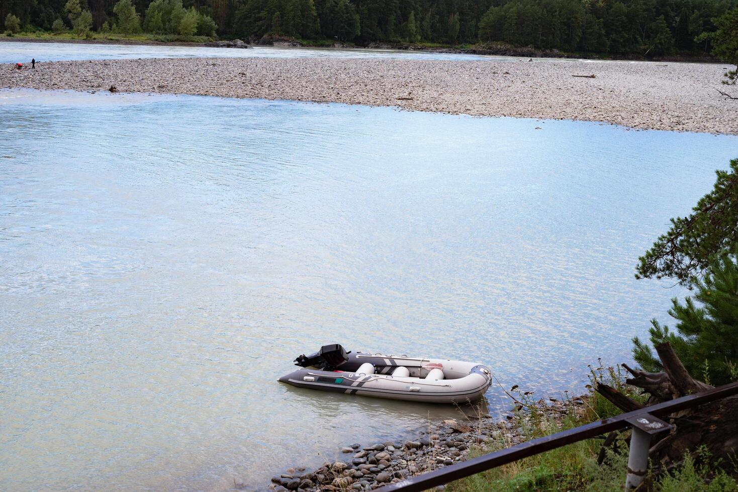 Inflatable boat moored on a serene riverbank with forest backdrop. photo