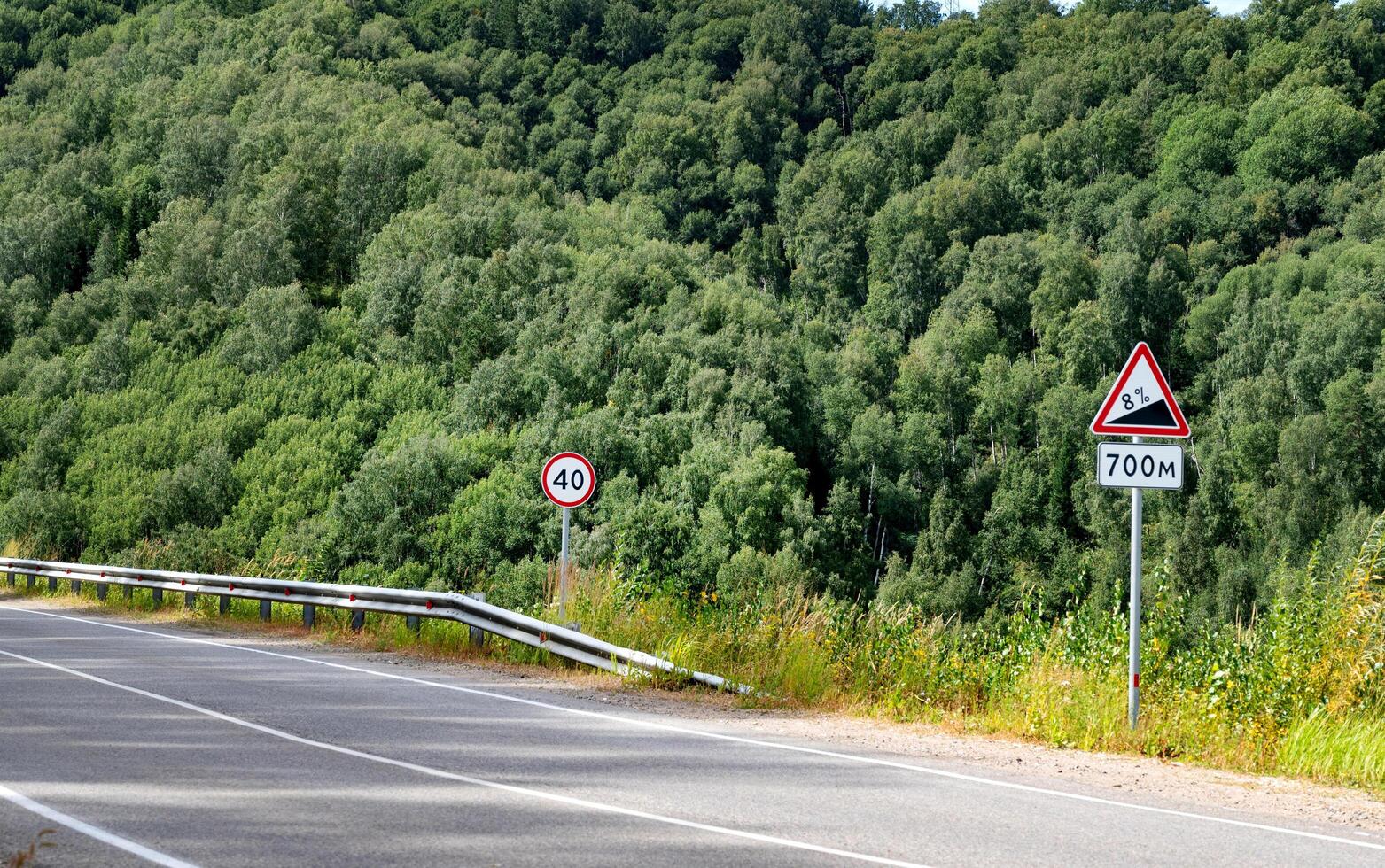 Road signs on a forested highway with speed limit and slope warnings. photo