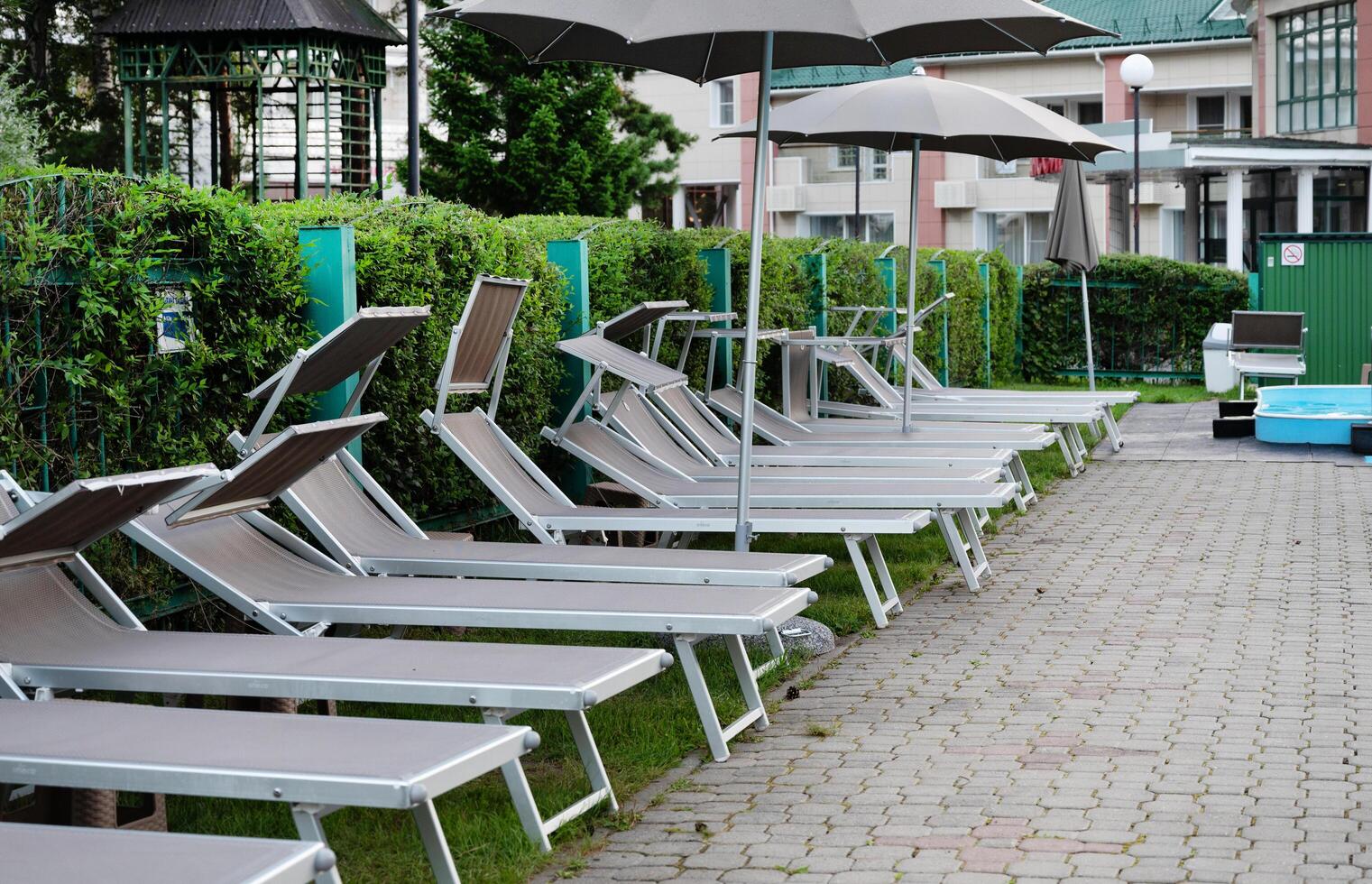 Four sleek, curved outdoor sun loungers made of woven material are positioned side by side on a tiled ground, ready for relaxation. photo
