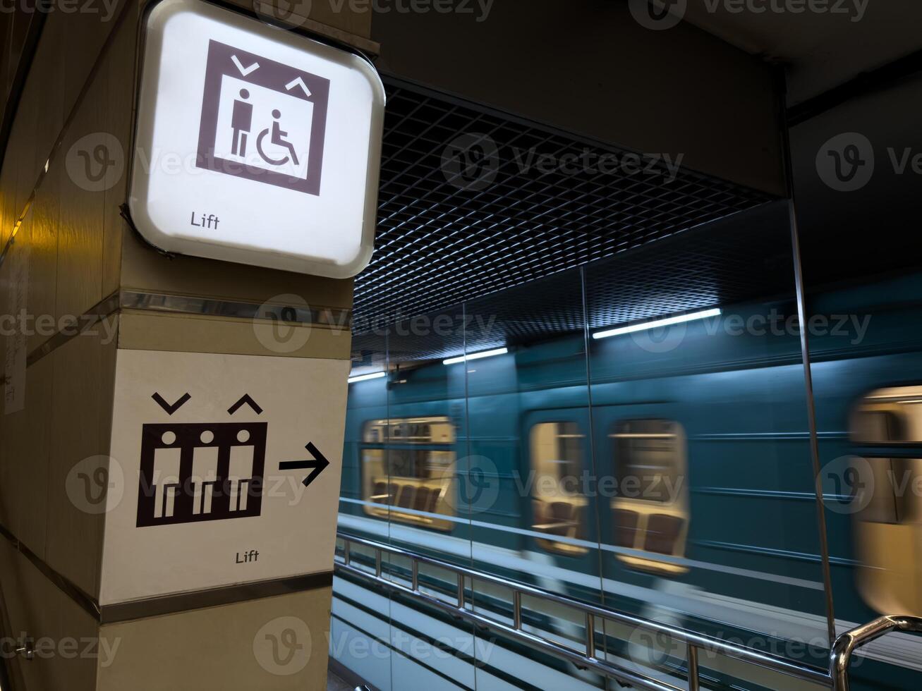 Modern metro station with moving train in the background and clear elevator signs for passengers including people with disabilities, promoting accessibility and public transport infrastructure photo