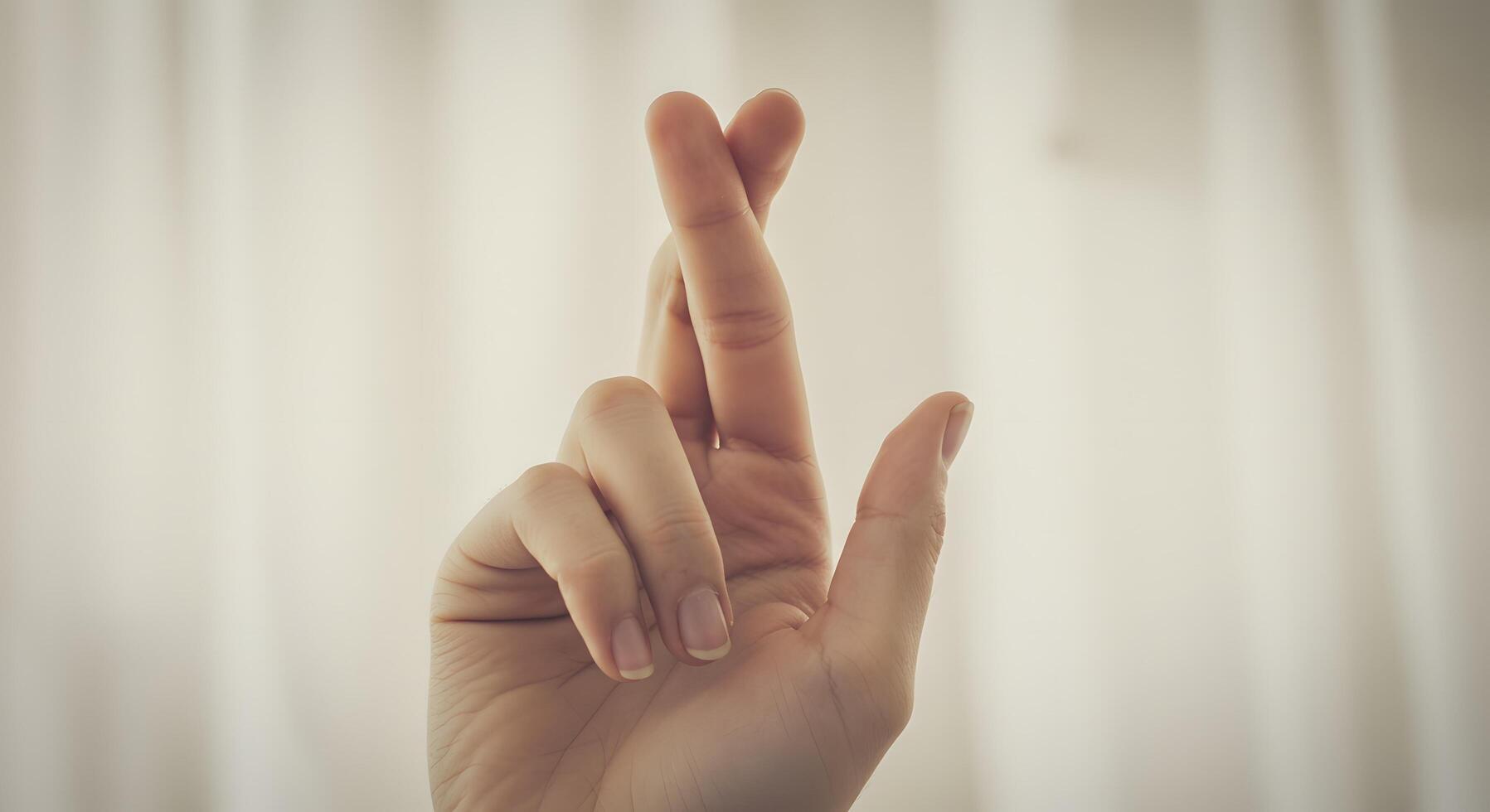 Fingers crossed, Close-up of a left hand with crossed fingers against a plain background, conveying luck, trust, or anticipation photo