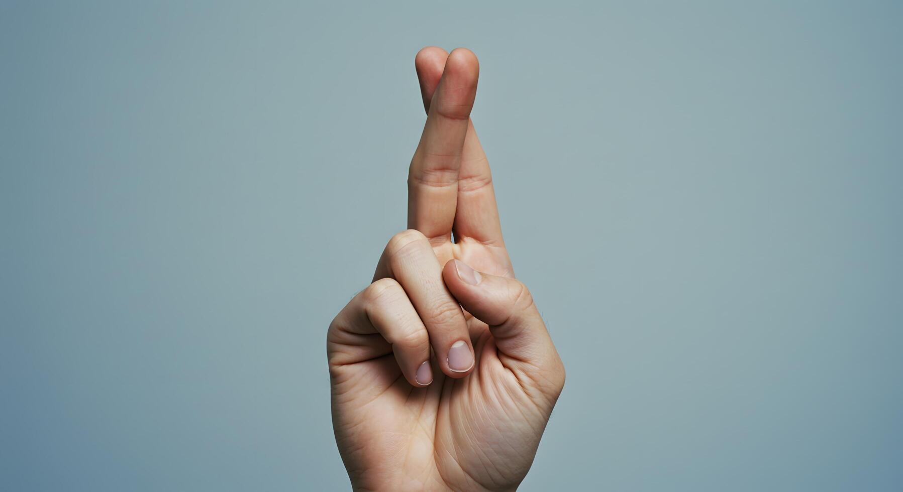 Fingers crossed, left hand making a fingers-crossed gesture on a minimalist backdrop, photo