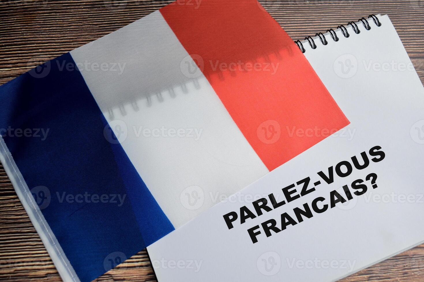 Concept of with question parlez-vous francais write on book and flag of french isolated on Wooden Table. photo