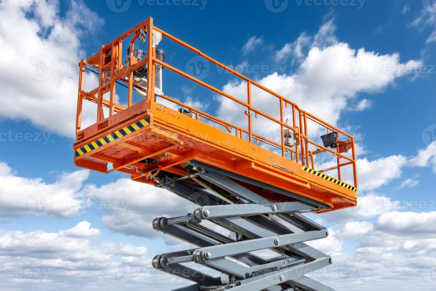 Scissor lift extended reaching high into blue sky with white clouds photo