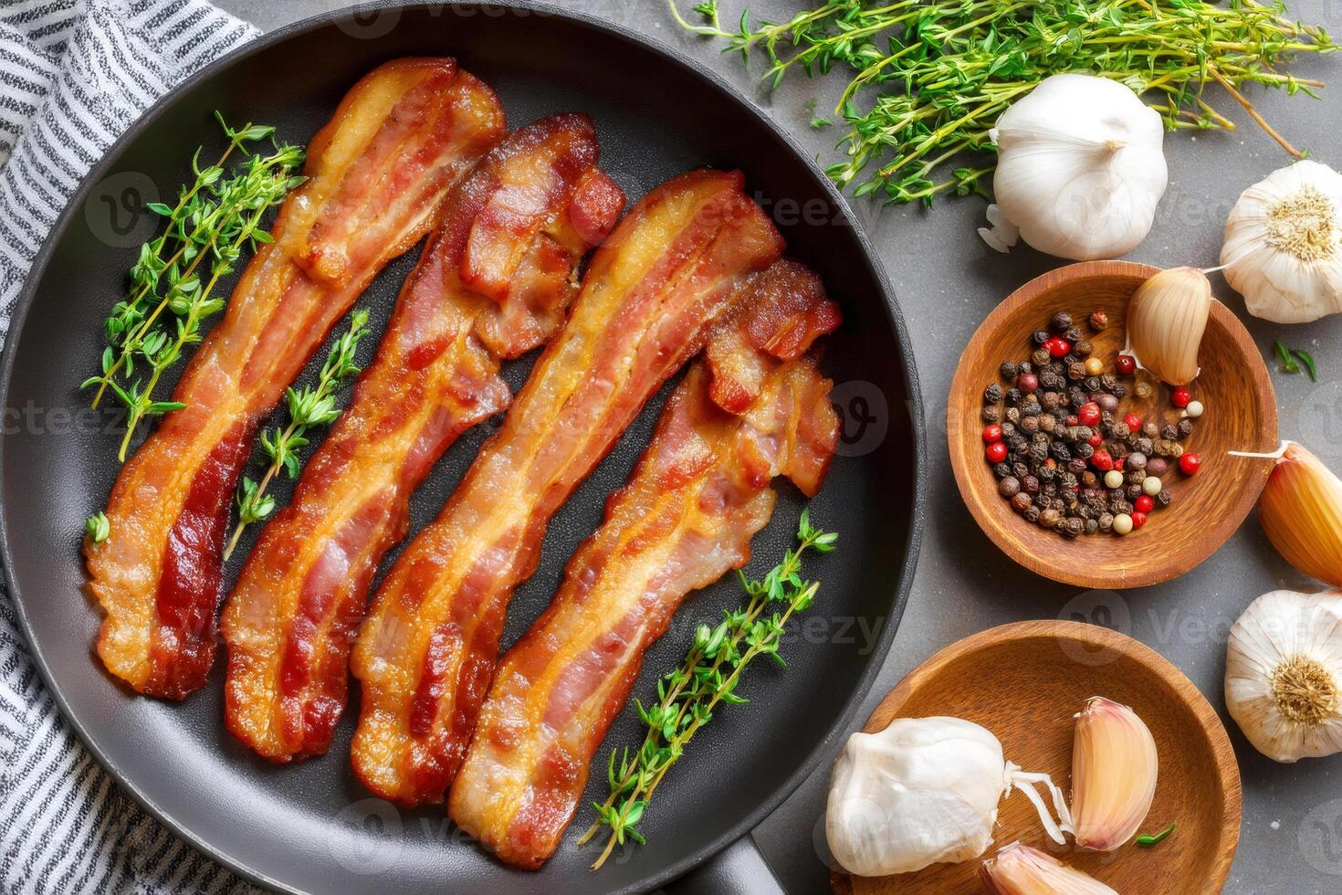 Fried bacon with thyme in pan and garlic with peppercorns on grey table photo