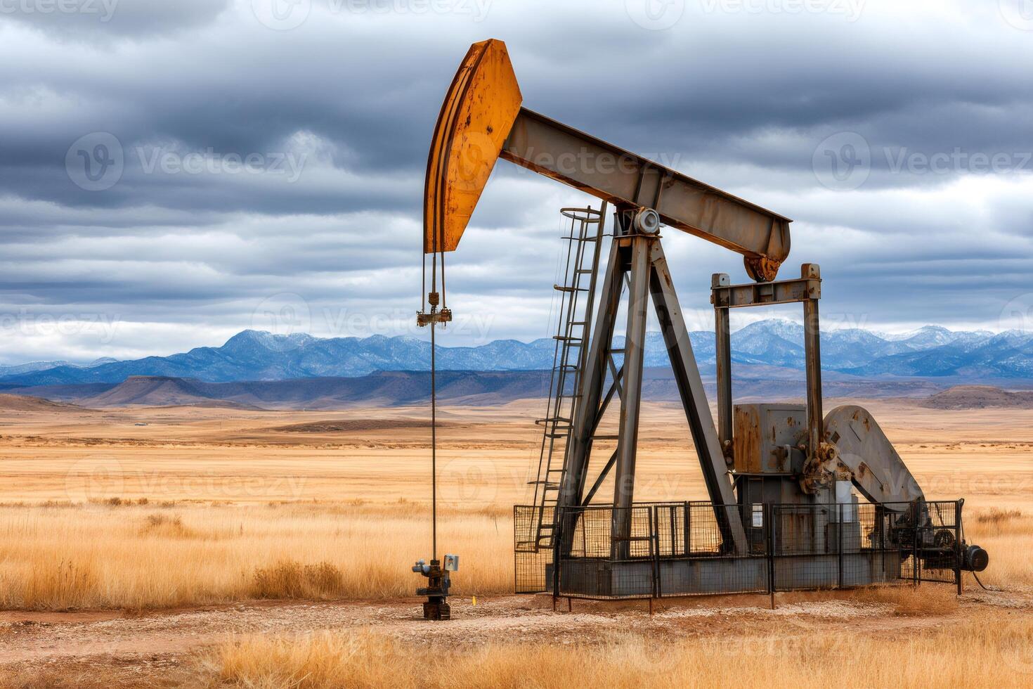 Pump jack extracting crude oil in a dry landscape with mountains and cloudy sky photo
