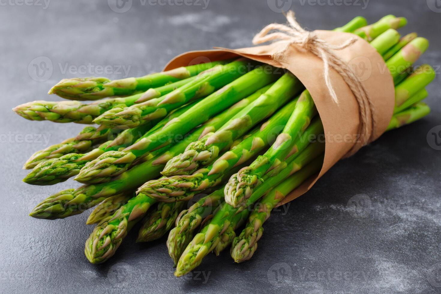 Bunch of fresh green asparagus wrapped in brown paper lying on dark background photo