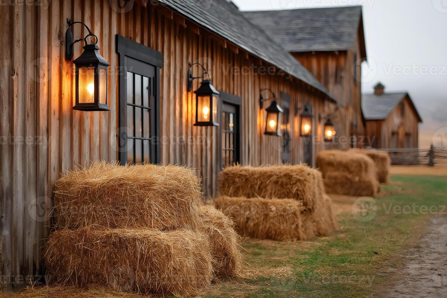 Hay bales resting against barn wall with lit lanterns at dusk photo