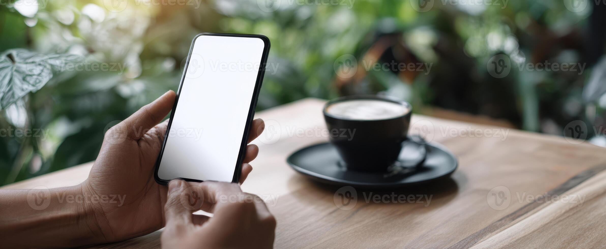 The smartphone held in hands with coffee on a wooden table. photo