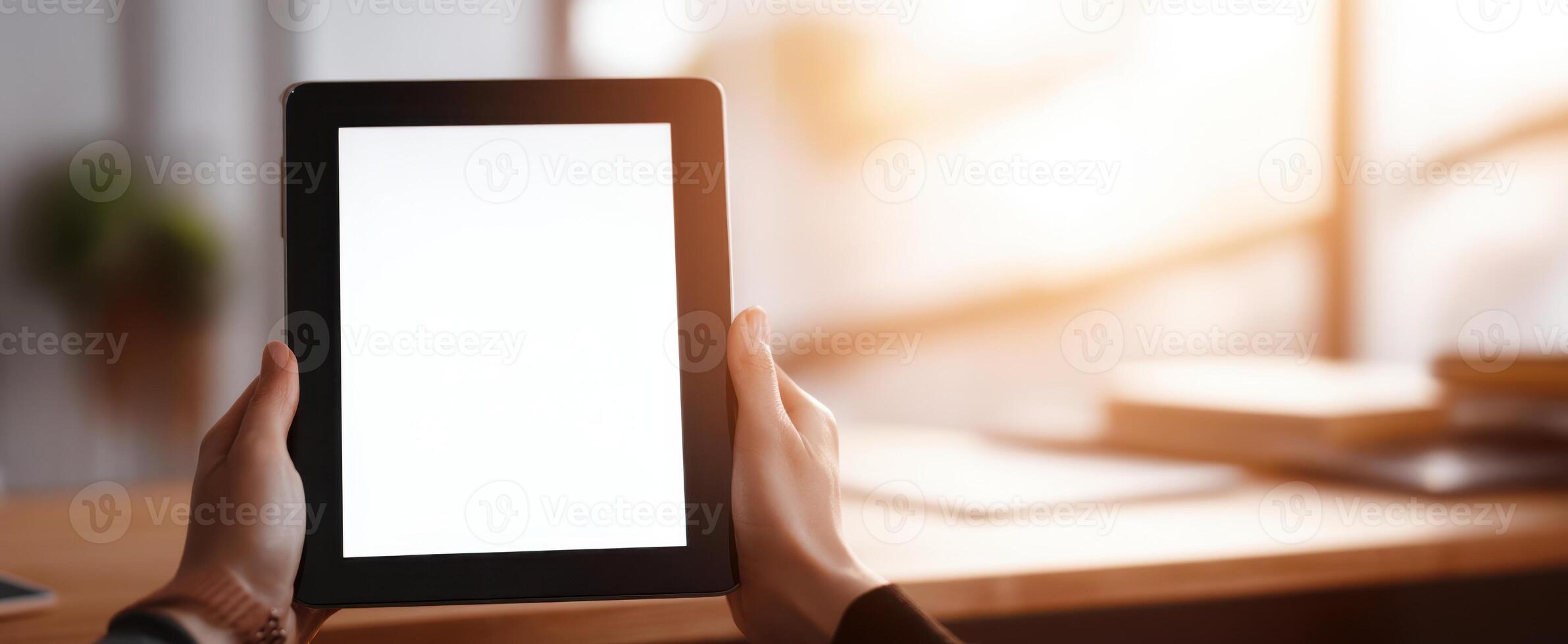 The hands holding a blank tablet in a bright modern workspace setting. photo