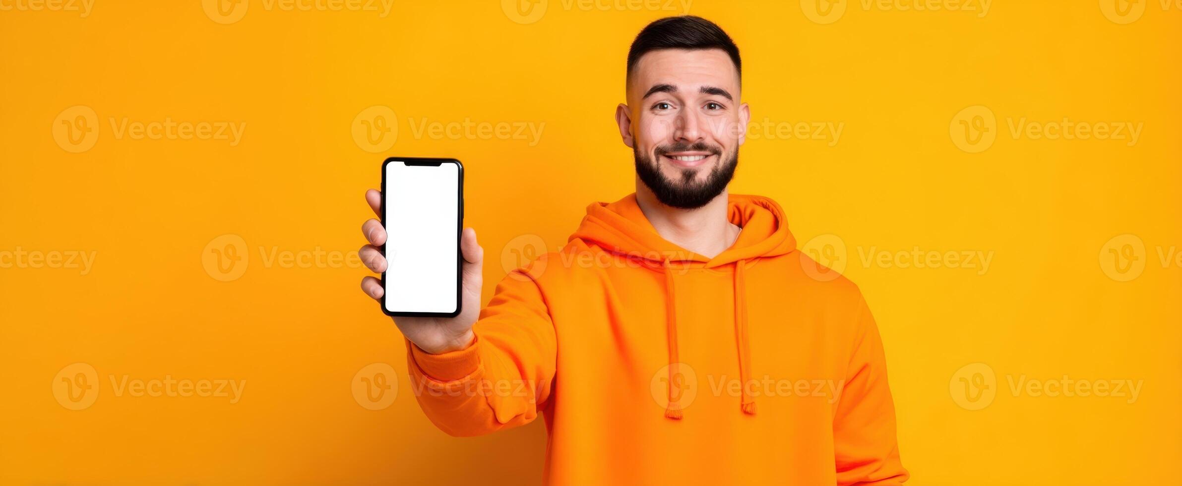 The smiling man showcasing a smartphone against a vibrant orange background photo