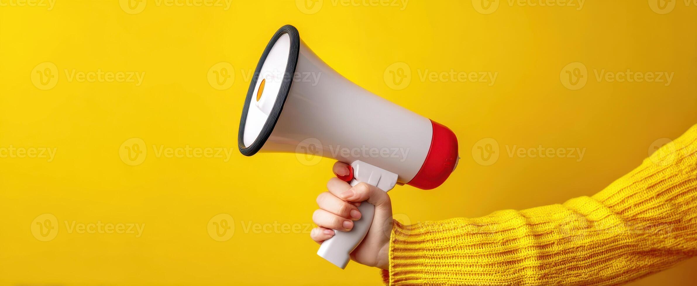 The megaphone being held in a vibrant yellow background for effective communication. photo