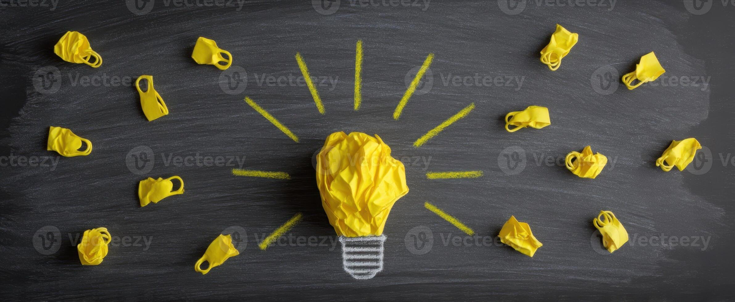 The innovative lightbulb surrounded by crumpled yellow paper ideas on a chalkboard. photo