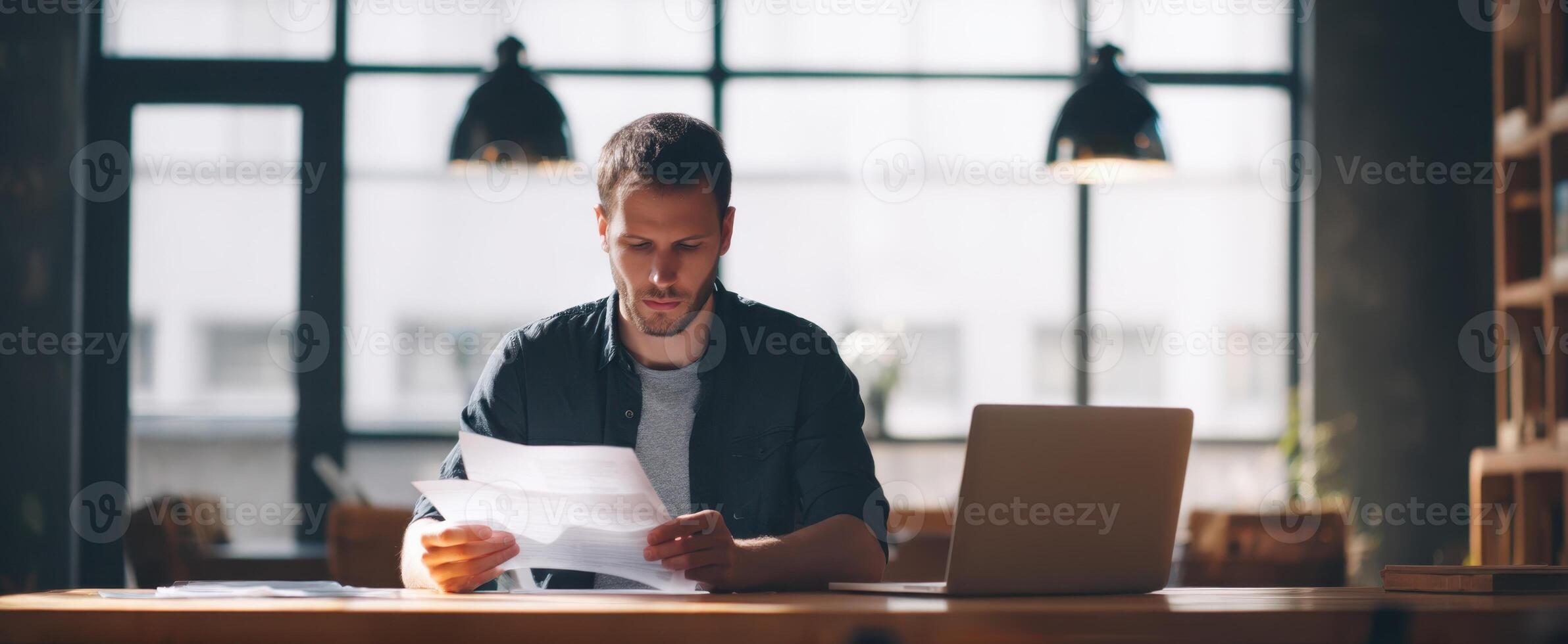 The man reading documents in a modern workspace with a laptop. photo