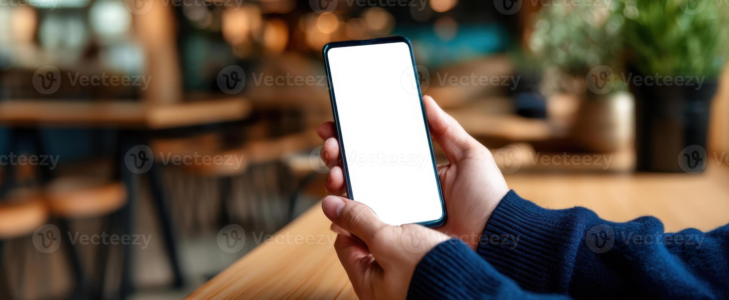 The modern smartphone held in hands with a blank screen in a cozy caf setting. photo