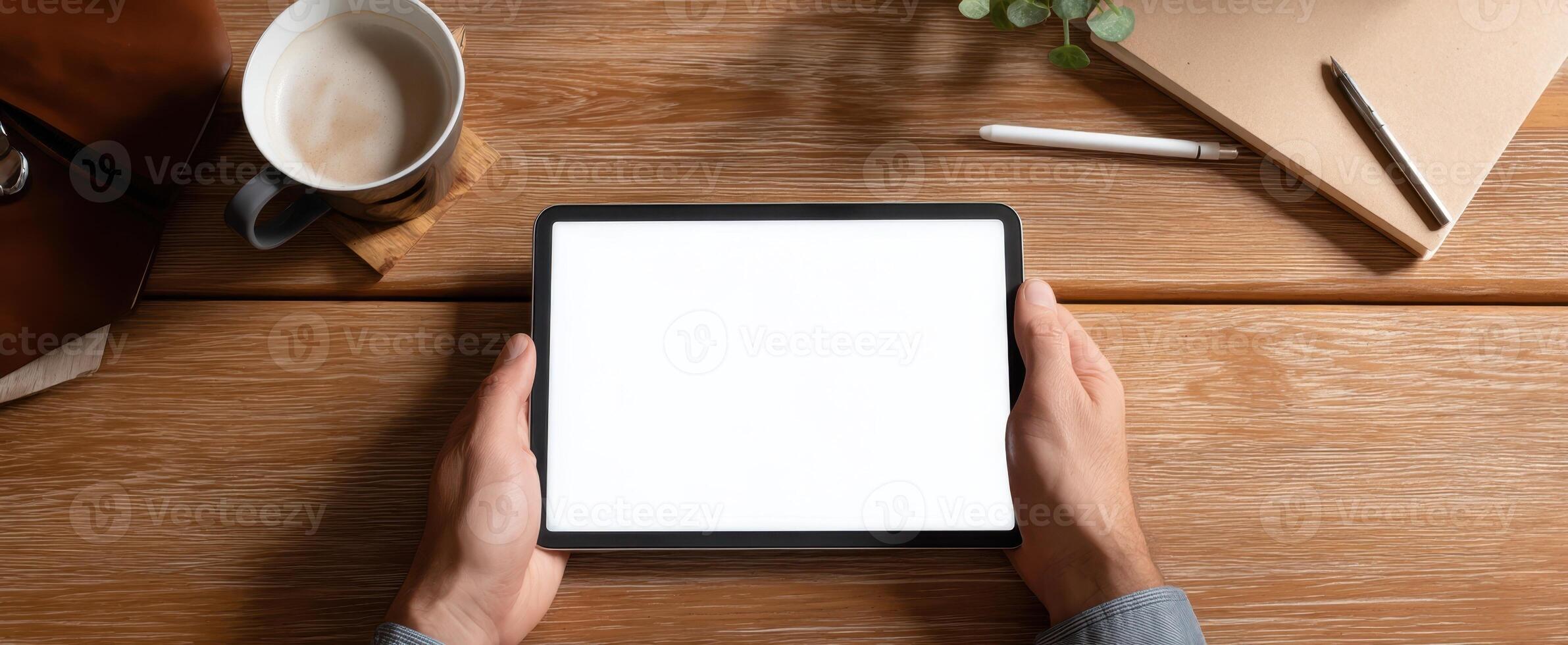 The tablet resting in hands against a rustic wooden workspace backdrop. photo