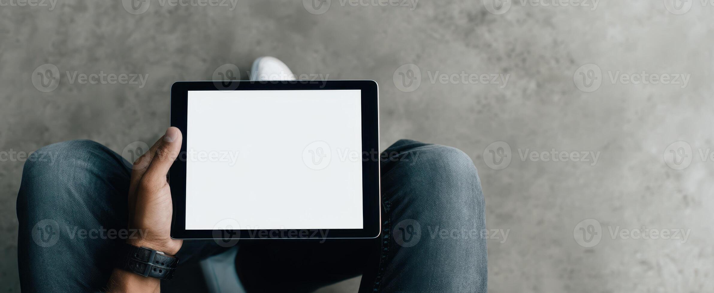 The tablet held by a person sitting on a minimalistic floor environment. photo