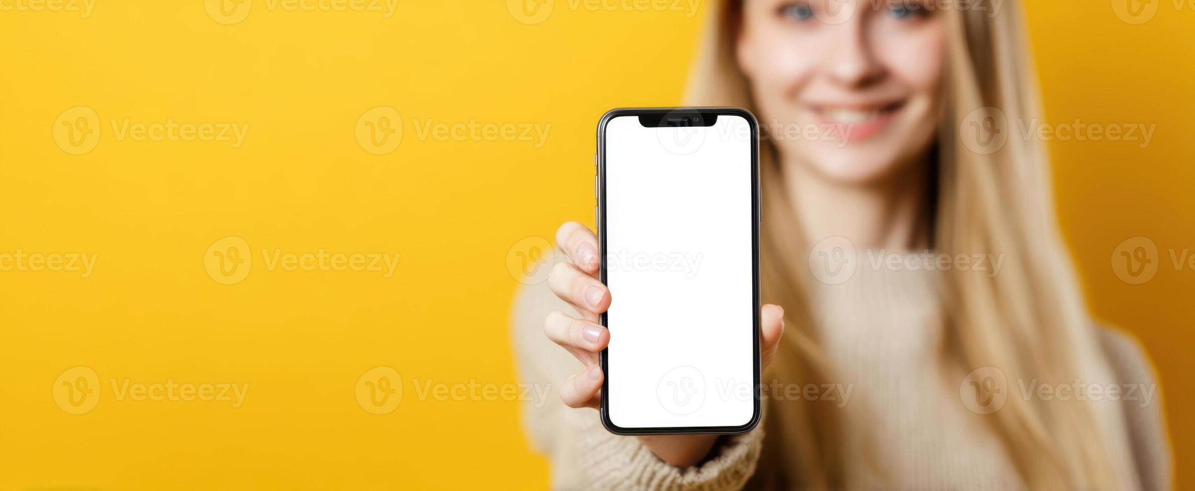 The smiling woman holding a smartphone with a blank screen on a yellow background photo