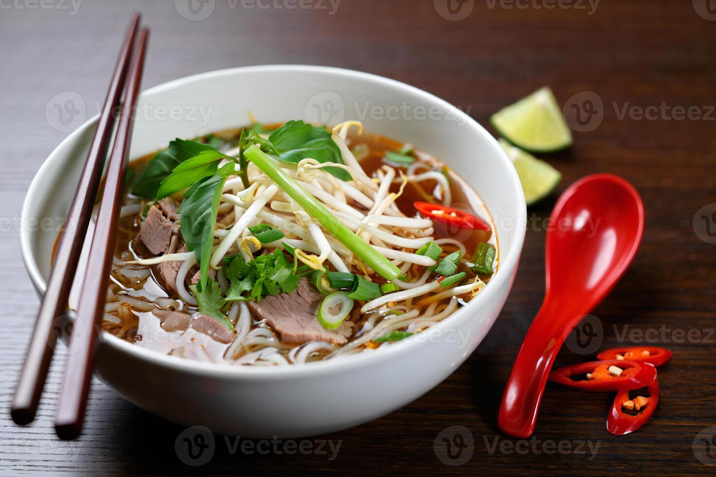A bowl of soup with chopsticks and a red spoon photo