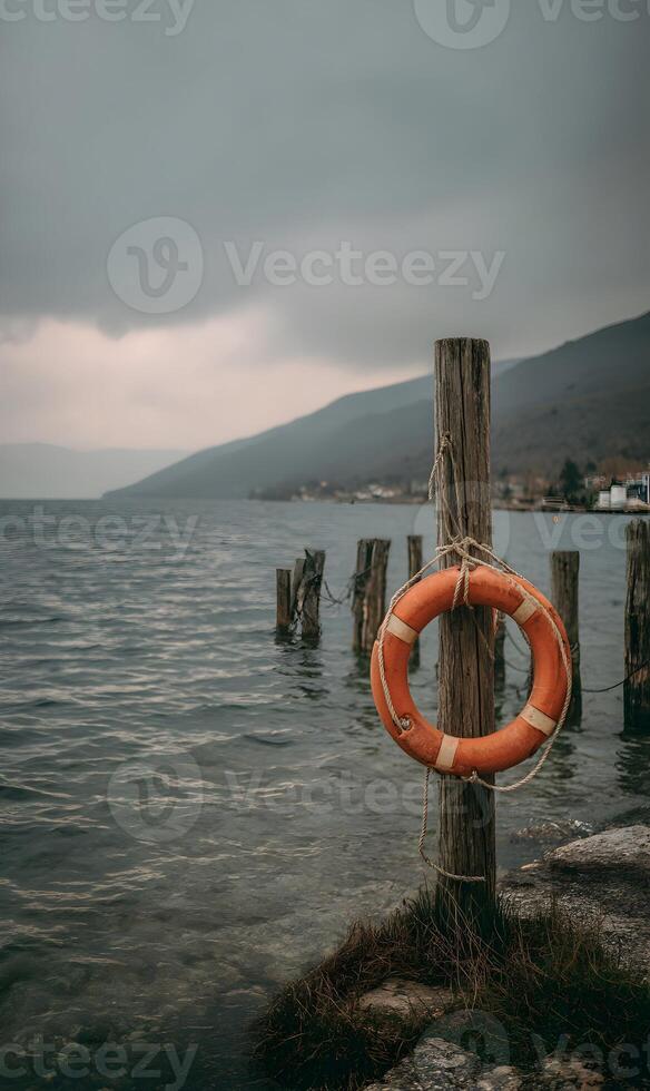 Lifeguard orange floatation device hanging on a wooden post at the water's edge on an overcast day photo