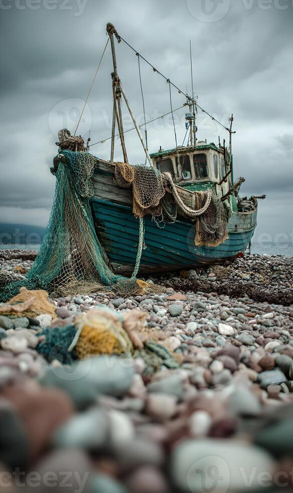 Abandoned fishing boat stranded on pebble beach under a dramatic cloudy sky creating moody atmosphere photo