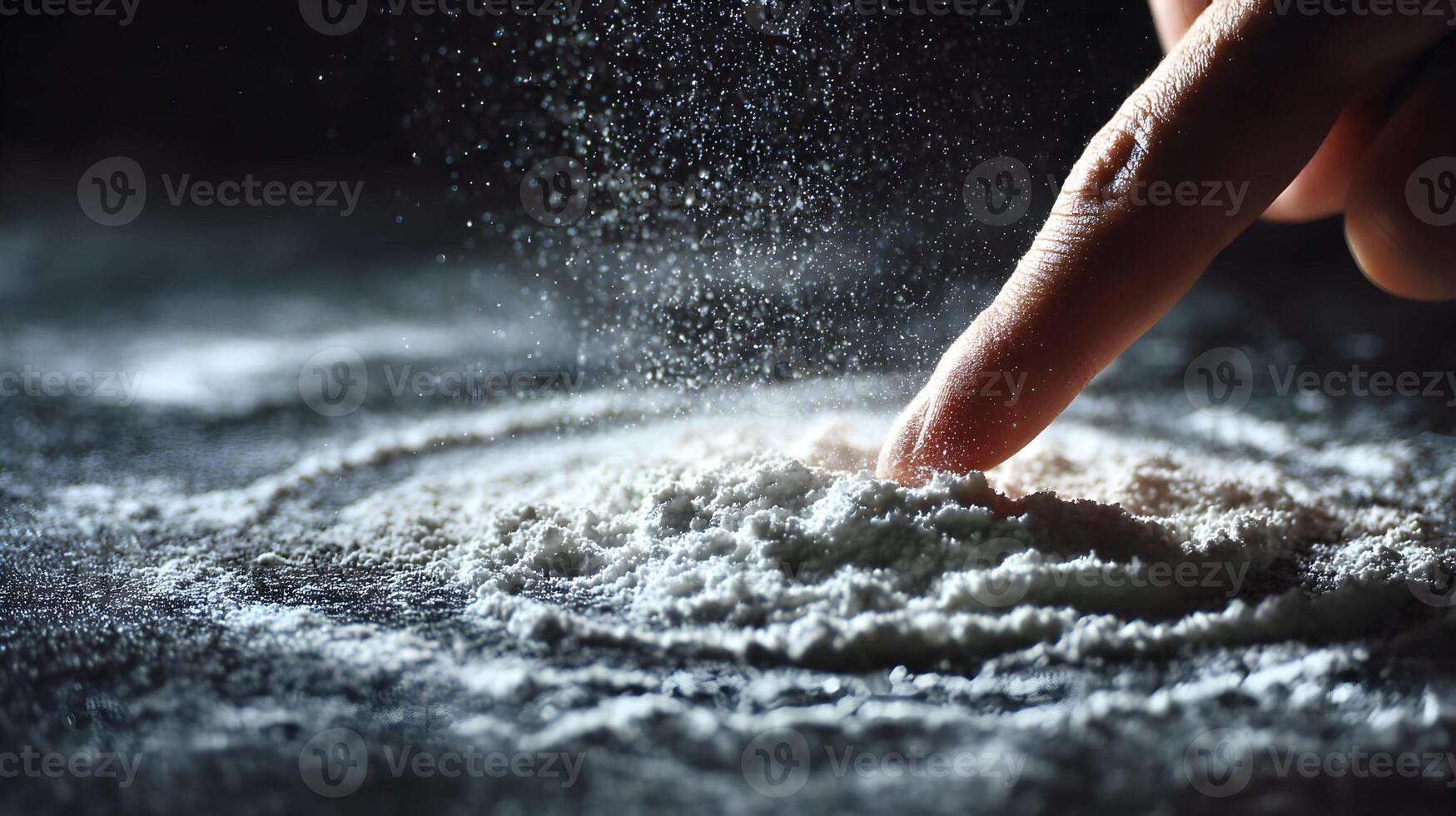 A finger touches a mound of white powder causing a cloud of particles against a dark surface photo