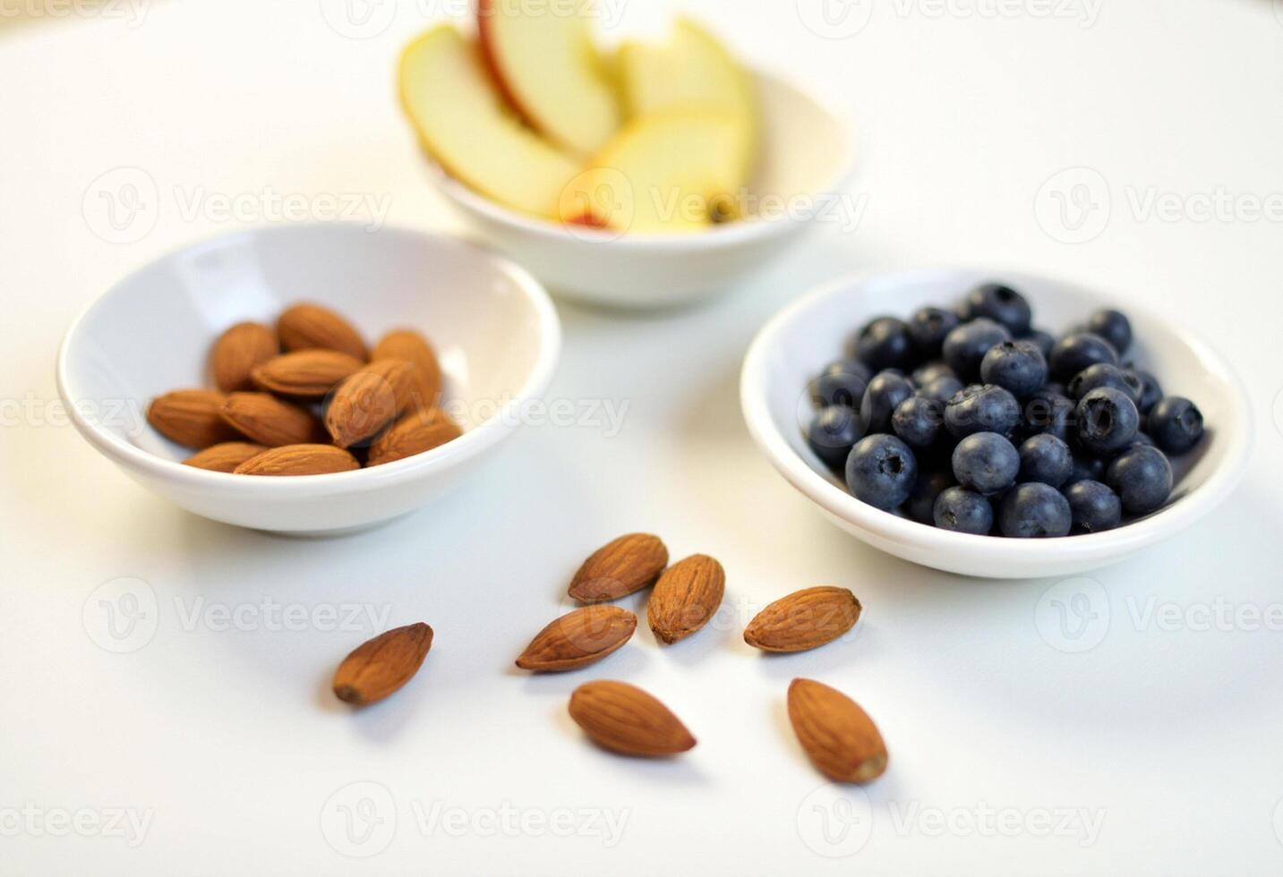 Three bowls of nuts and fruit on a white table photo