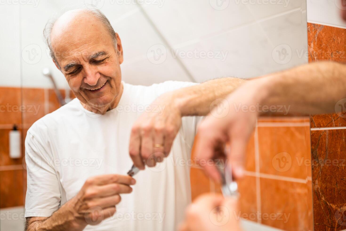 Elderly caucasian man grooming in the bathroom, trimming fingernails with a clipper with his reflection visible in mirror. photo