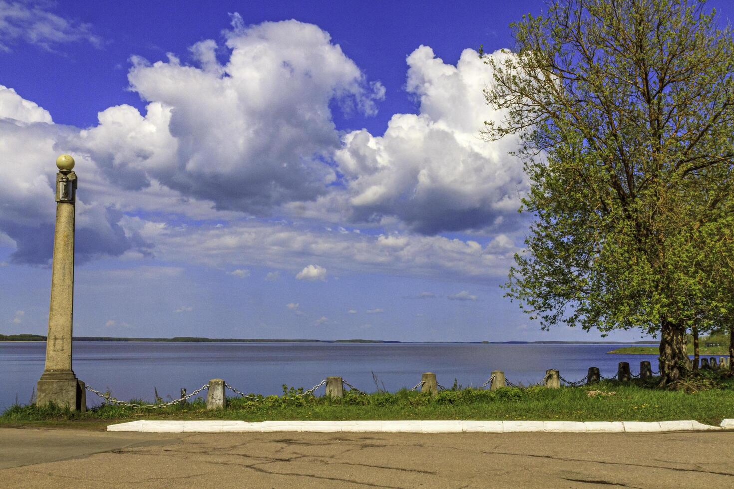 Peaceful river bank with an old lamp post and tree under a blue sky. photo