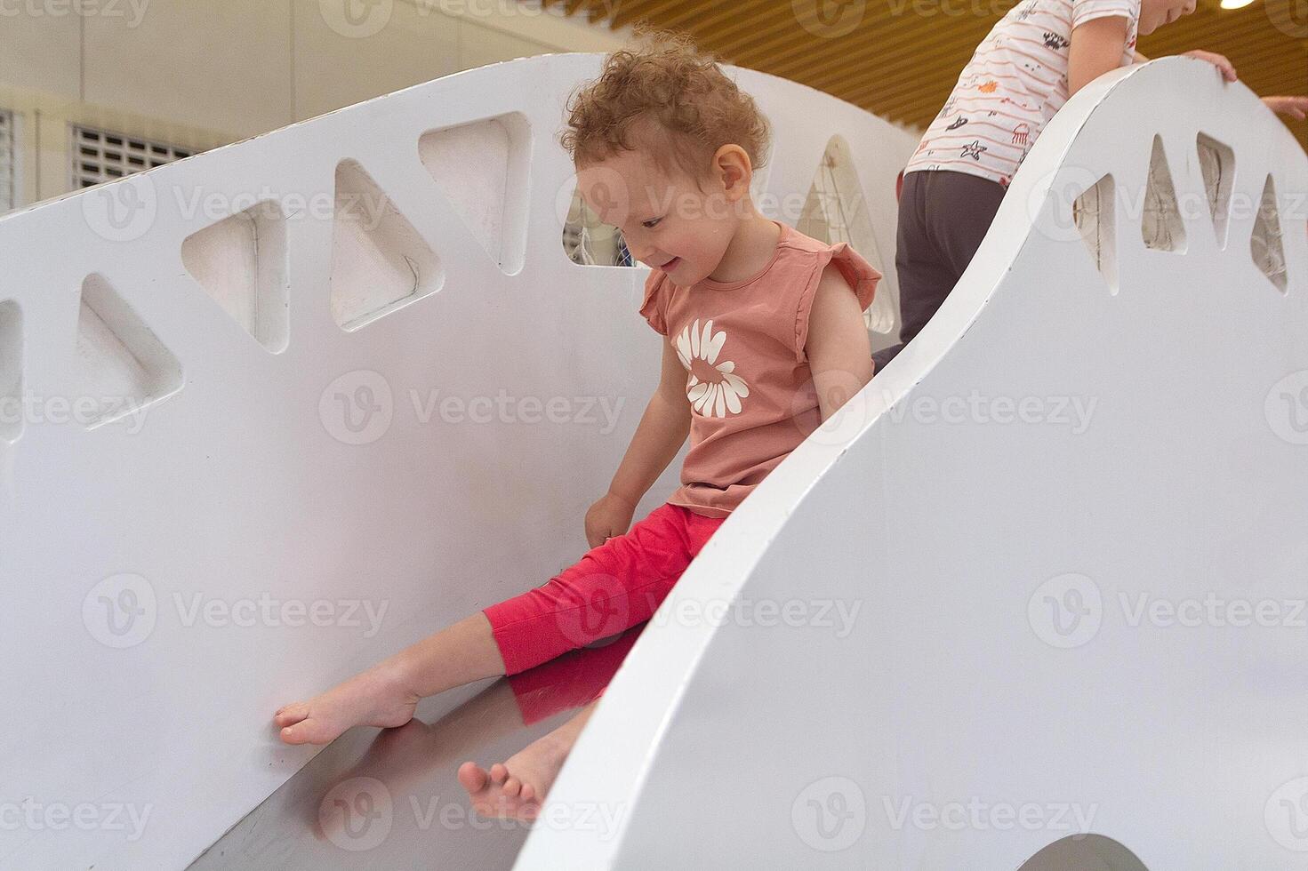 A pretty curly child plays a slide in a game center, photo