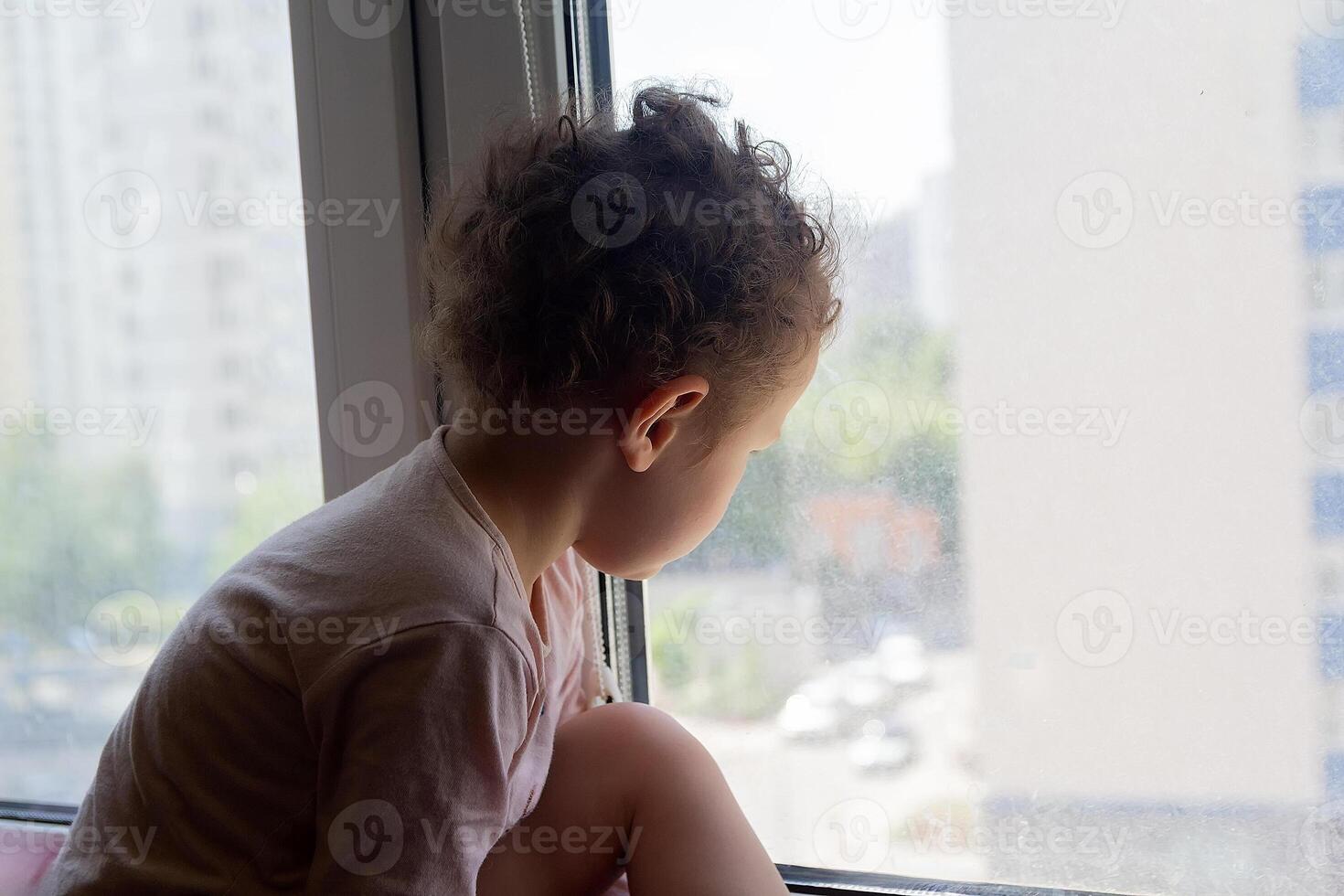 A sad child looks out the window. People photo